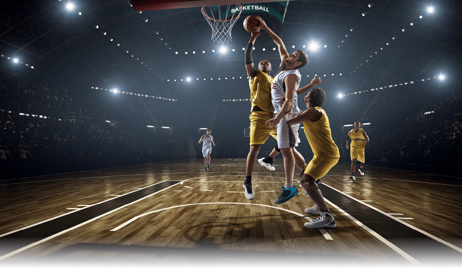 Low angle view of a professional basketball game  A player is in mid air holding ball about to score a slam dunk, but the player from the opposite team is ready to block him   A  game is in a indoor floodlit basketball arena  All players are wearing generic unbranded basketball uniform 