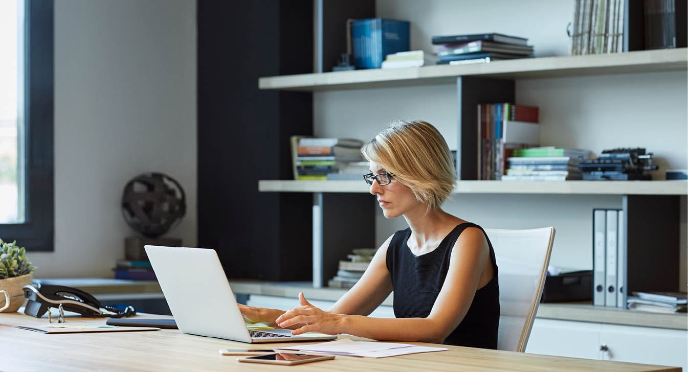 Businesswoman using laptop at desk  Confident female professional is working in textile factory  Executive is with short brown hair 