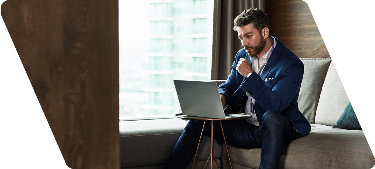 Man working away from home on business trip sitting on sofa and concentrating, looking at screen, contemplation, serious, planning